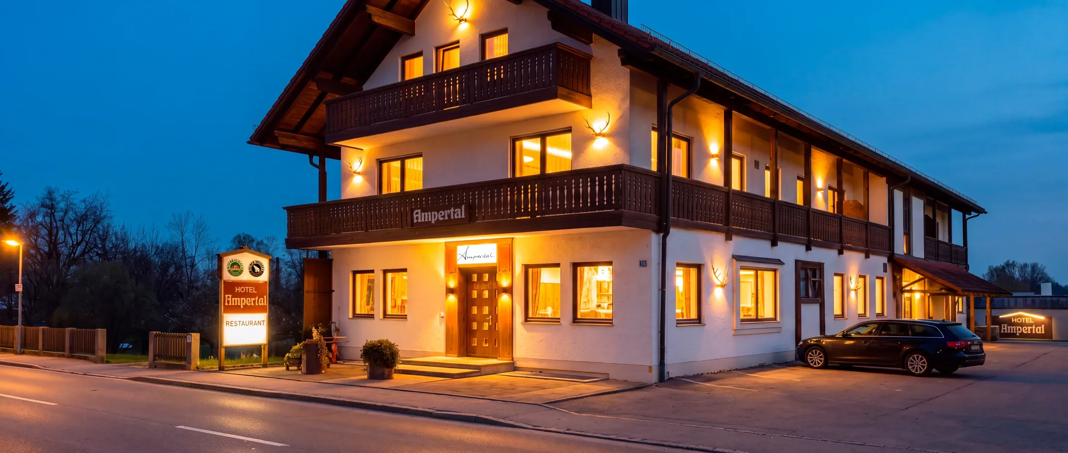 Das Hotel Restaurant Ampertal am Abend: beleuchtete Fassade mit Balkonen und Ampertal-Schriftzug
